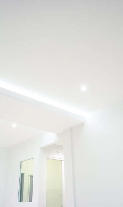 LED strip light and illumination. Also called ribbon light or LED tape. That suspended on ceiling and hide in plasterboard in empty living room include down light, white wall, window, air conditioner, adjusting vertical or venetian blinds. That is modern luxury interior home building design and technology.